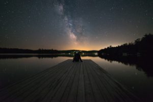 Man sitting on a dock under a night sky.